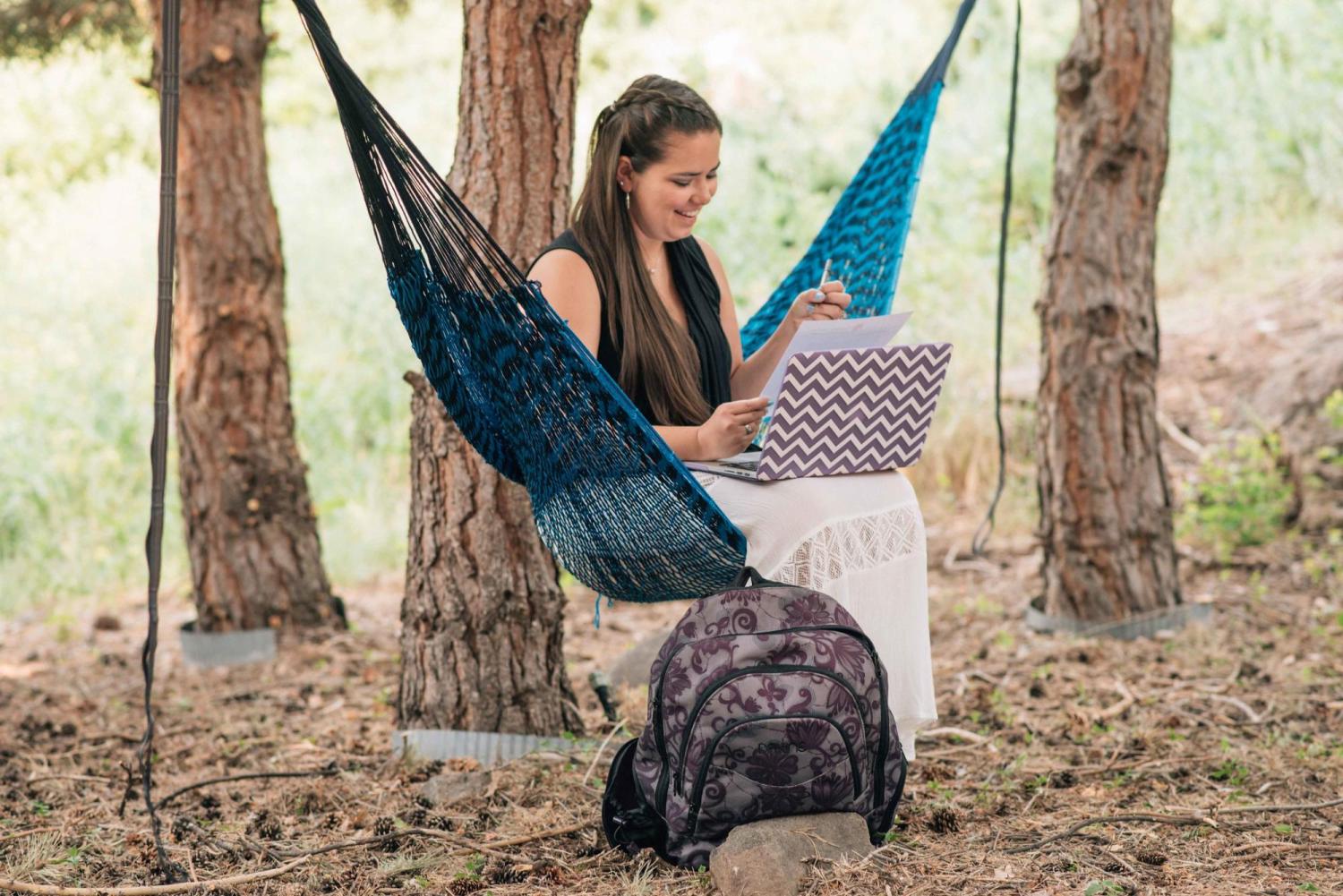 A student sits in a hammock outside while working on her laptop