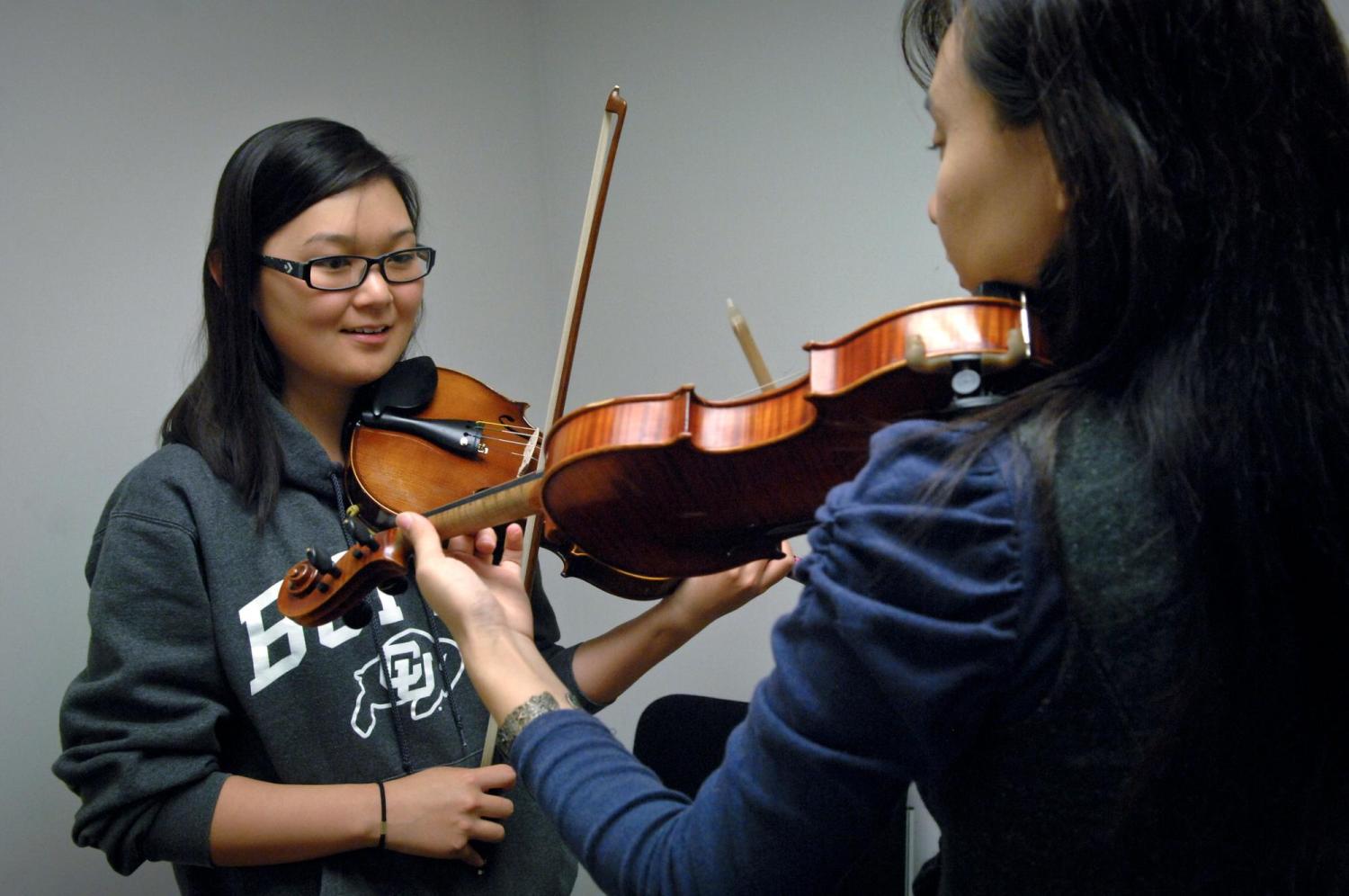 A violin student watches as her teacher demonstrates on her violin