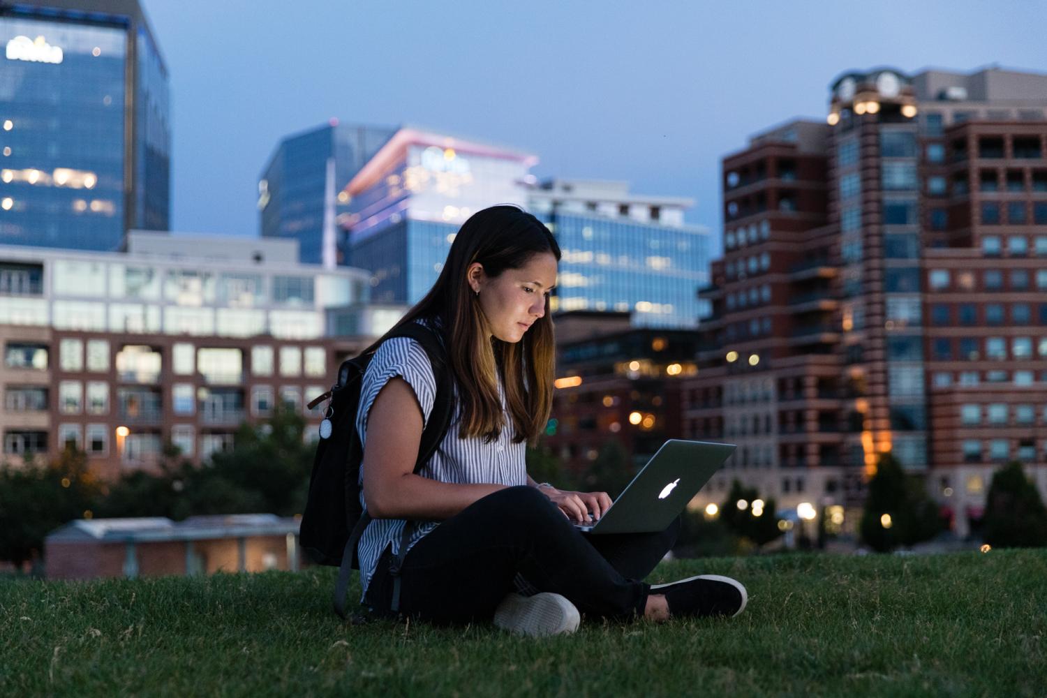 A student works on her laptop outside with the evening Denver skyline in the background
