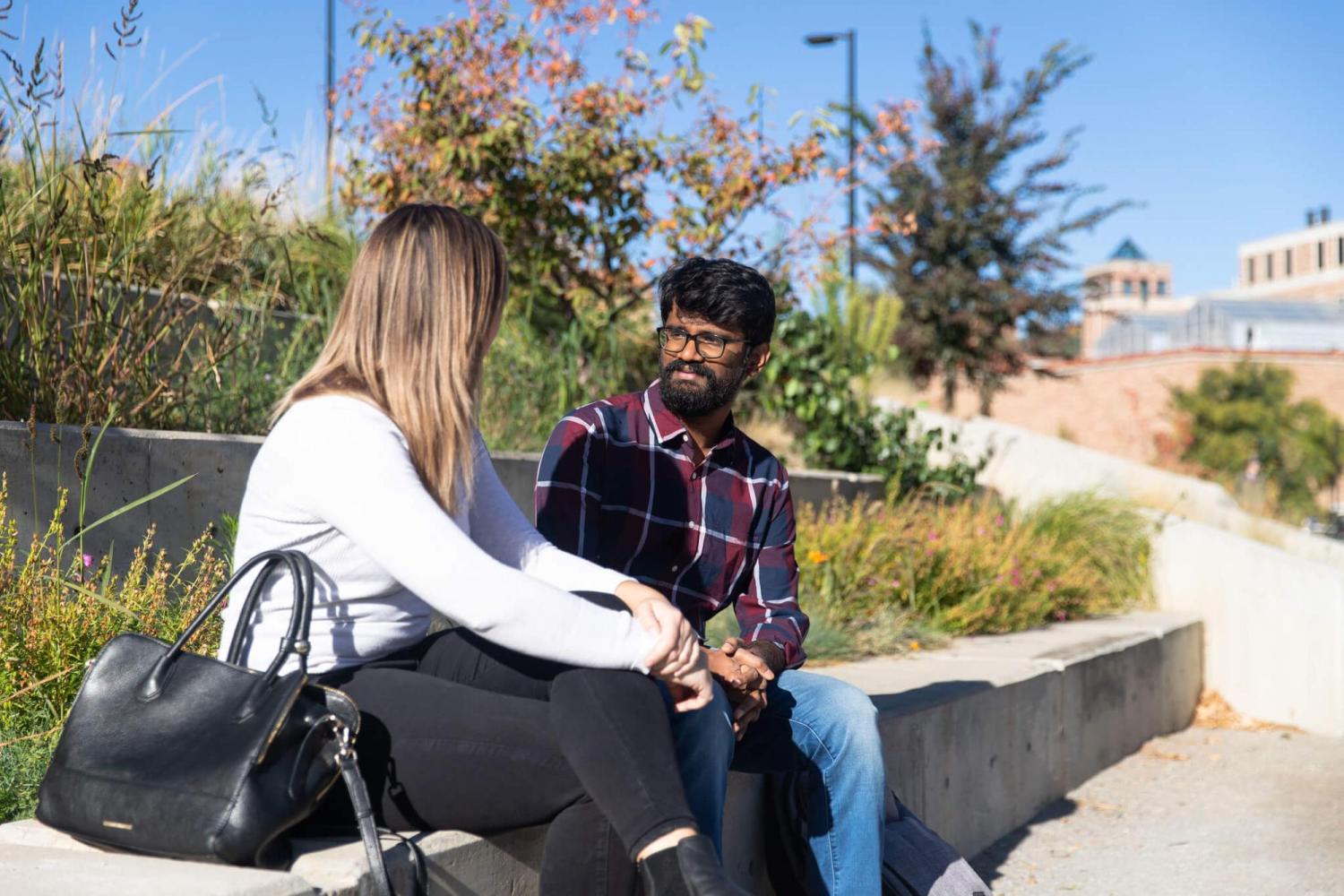 A man and a woman sit outside on campus talking