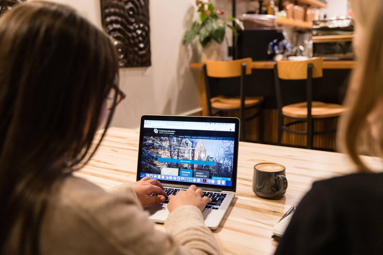 A student browses the Continuing Education website at a cafe with a coffee on her table
