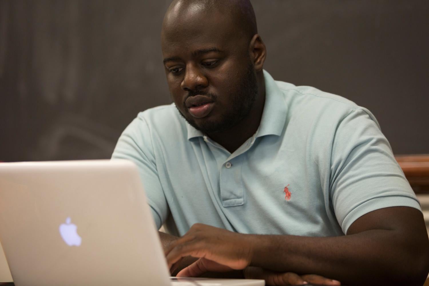 A man in a polo shirt browses on his apple laptop