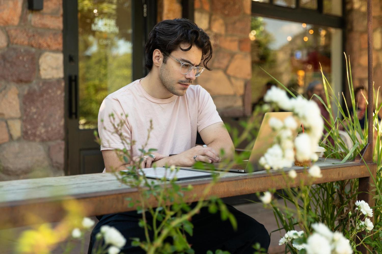 A student works on his laptop on a cafe patio