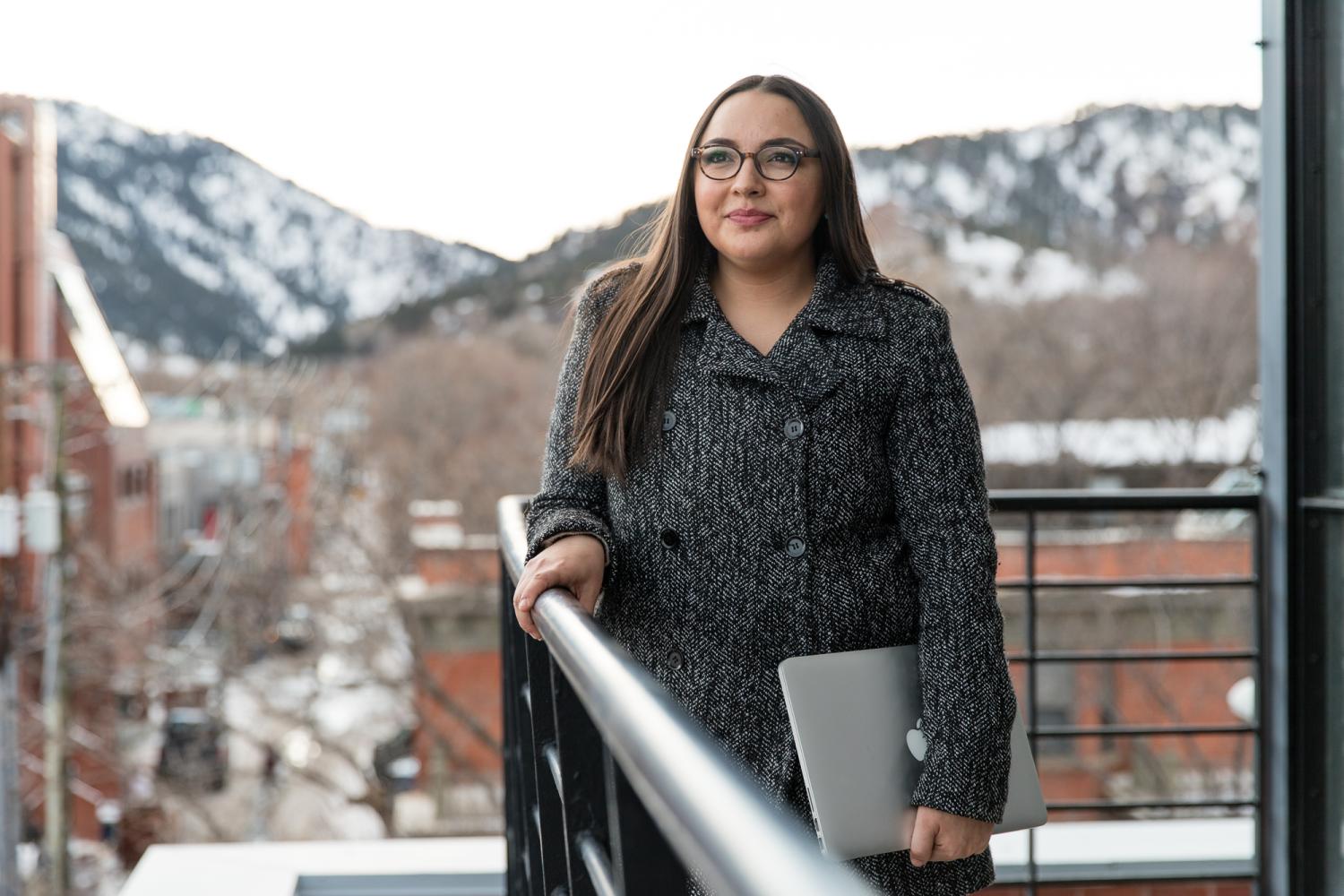 A student poses outside on a balcony with the snowy Boulder foothills in the background