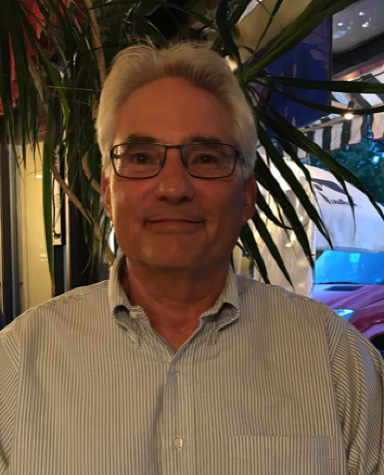 Headshot of man with blue striped polo, glasses, and gray hair