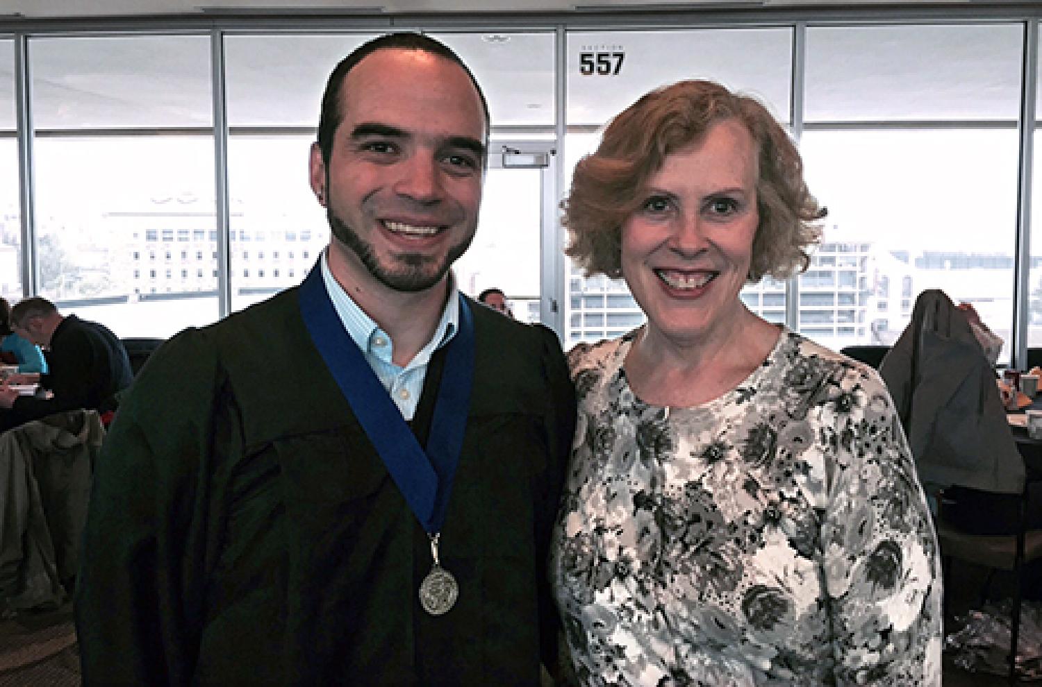 man with blue ribbon award around his neck standing with woman in floral blouse