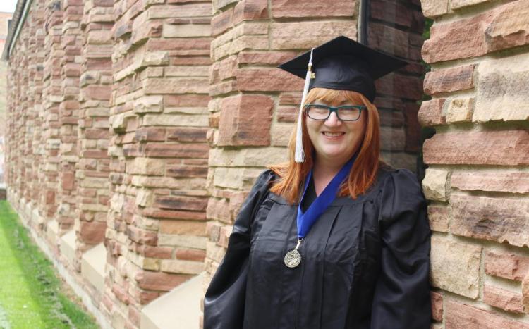 Red head woman with graduation cap and gown posing in front of brick building
