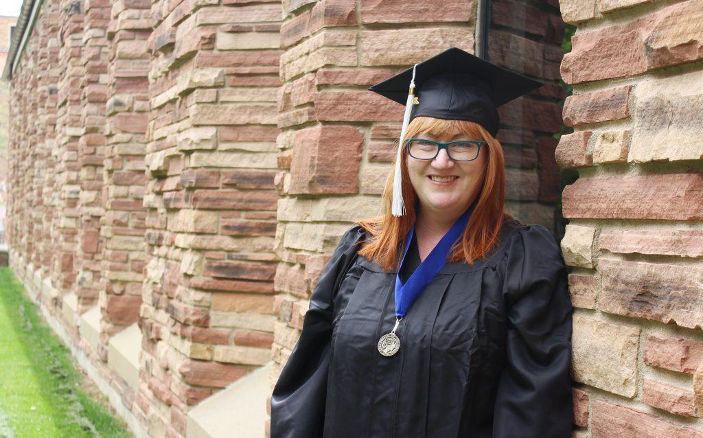 Red head woman with graduation cap and gown posing in front of brick building
